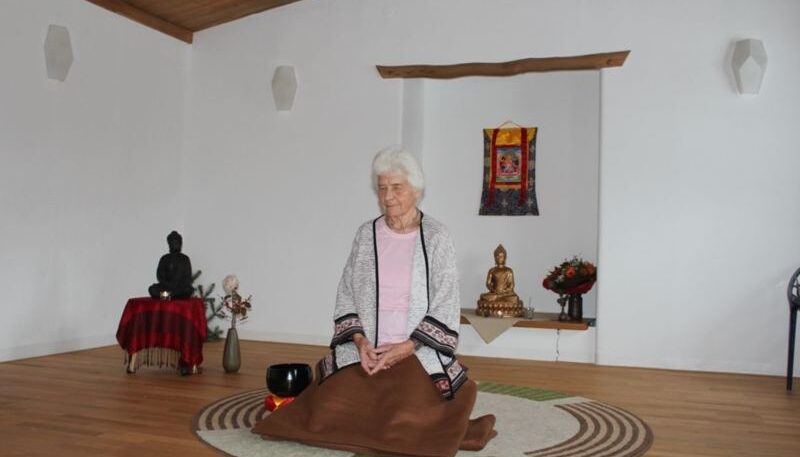 Ältere Frau meditiert in ruhigem Raum.