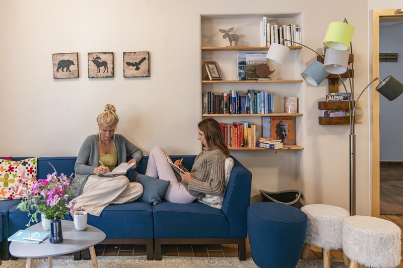 2 frauen sitzen auf einer couch und schreiben in ein buch